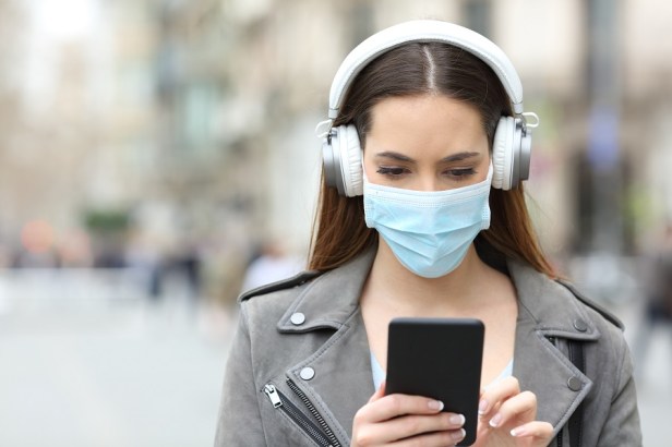 Girl with mask and headphones reads phone in the street